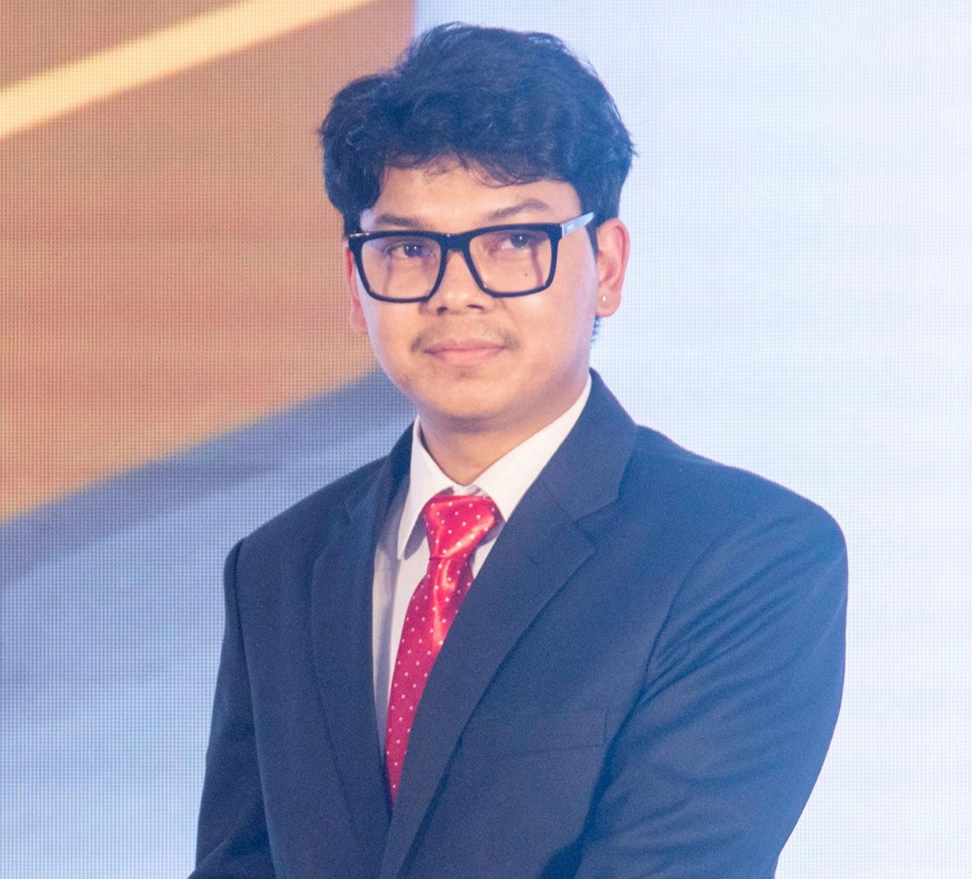 Abinash Adhikari in a dark suit and red tie, on stage